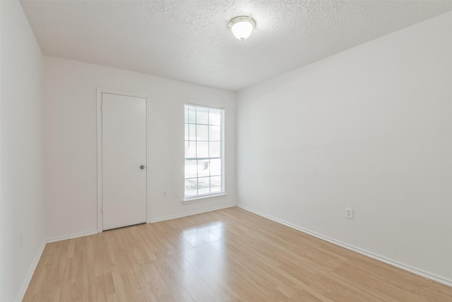 spare room featuring a textured ceiling, light wood finished floors, and baseboards