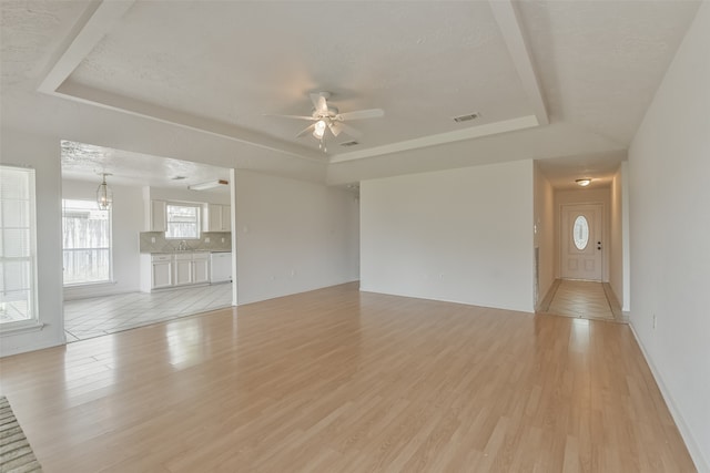 unfurnished living room featuring ceiling fan, a raised ceiling, and light tile patterned floors