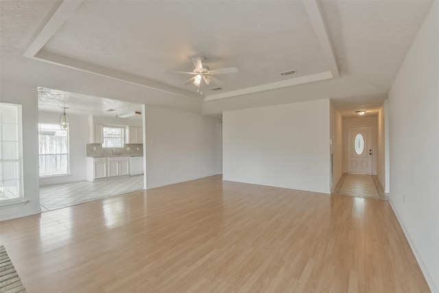 unfurnished living room with light wood-style flooring, a tray ceiling, and ceiling fan with notable chandelier