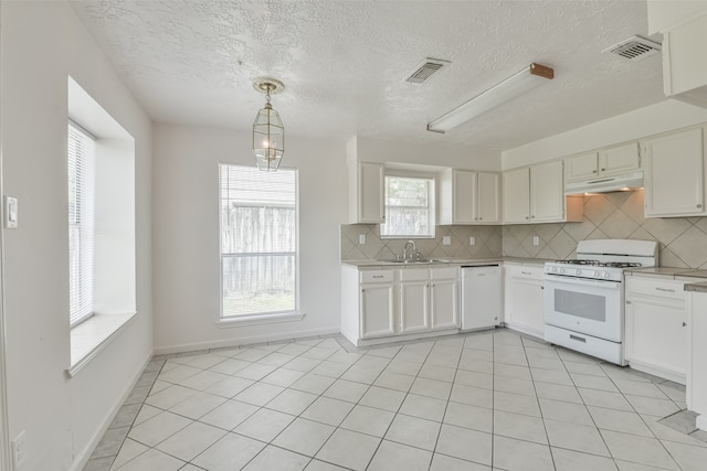 kitchen with a wealth of natural light, white appliances, light tile patterned floors, and backsplash