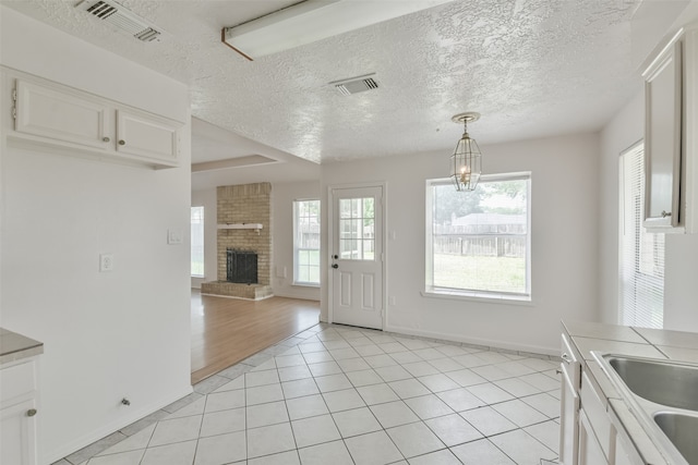 unfurnished dining area with an inviting chandelier, a textured ceiling, a brick fireplace, and light hardwood / wood-style floors