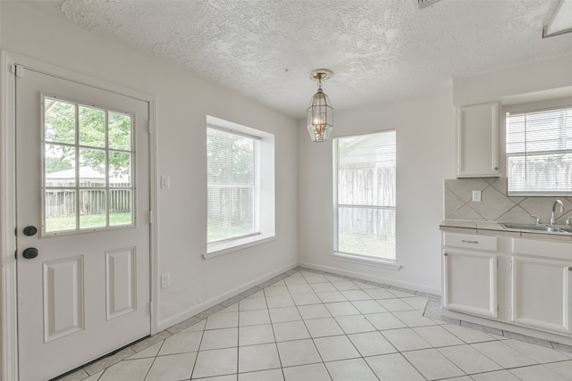 unfurnished dining area featuring light tile patterned floors, sink, plenty of natural light, and a textured ceiling