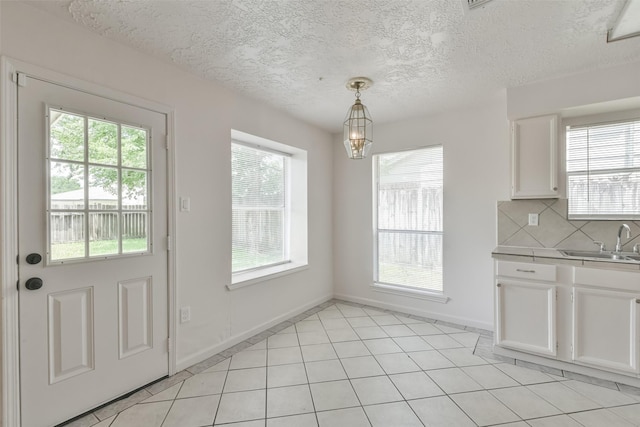 interior space featuring baseboards, an inviting chandelier, a textured ceiling, a sink, and light tile patterned flooring