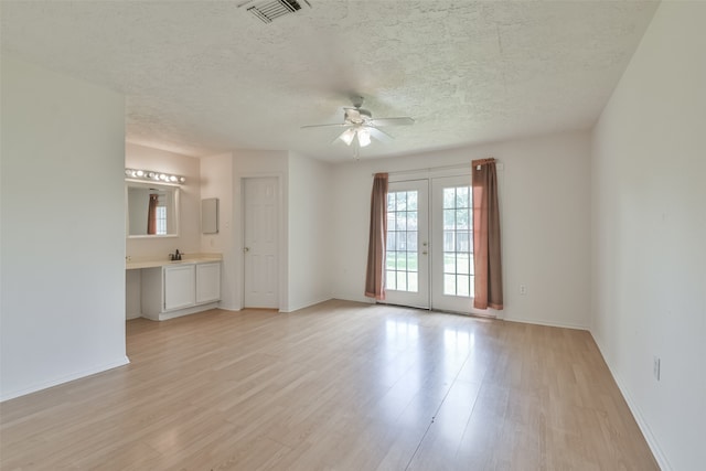 unfurnished living room with french doors, sink, light wood-type flooring, a textured ceiling, and ceiling fan