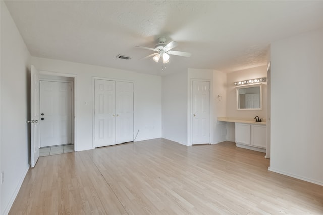 unfurnished bedroom with ceiling fan, connected bathroom, multiple closets, and light hardwood / wood-style floors