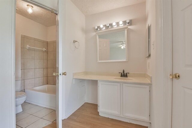 full bathroom with hardwood / wood-style flooring, tiled shower / bath combo, a textured ceiling, vanity, and toilet