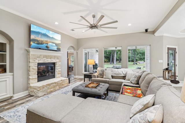 living room featuring a fireplace, ceiling fan, ornamental molding, and light wood-type flooring