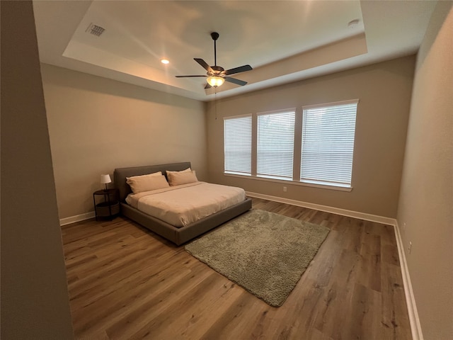 bedroom featuring ceiling fan, a tray ceiling, and wood-type flooring