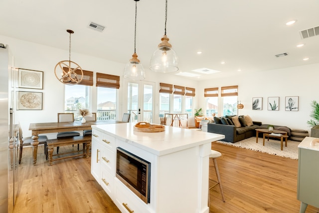 kitchen featuring a center island, white cabinetry, stainless steel microwave, and light wood-type flooring