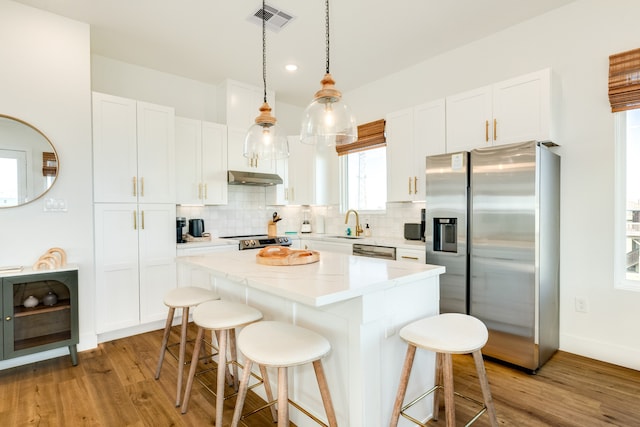 kitchen with decorative backsplash, appliances with stainless steel finishes, light hardwood / wood-style floors, and a kitchen island