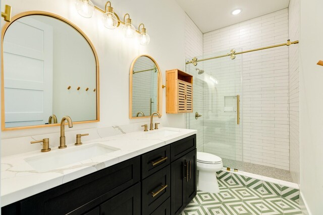 bathroom featuring a shower with shower door, toilet, dual bowl vanity, and tile patterned floors