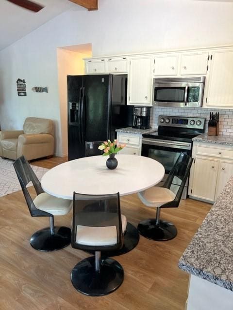 kitchen with tasteful backsplash, light wood-style flooring, vaulted ceiling with beams, light stone countertops, and stainless steel appliances