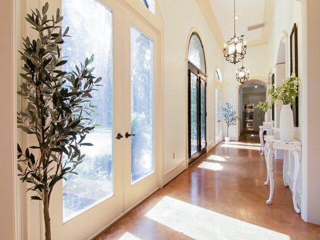 entryway with concrete flooring, ornamental molding, an inviting chandelier, and french doors