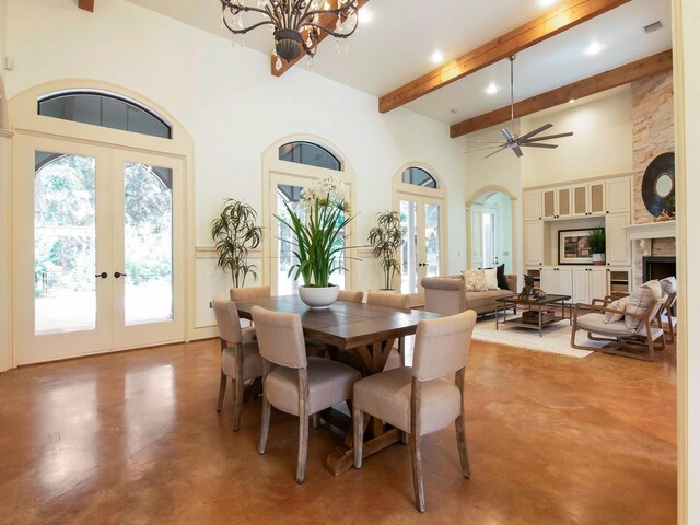 dining room featuring a fireplace, french doors, ceiling fan with notable chandelier, and concrete floors