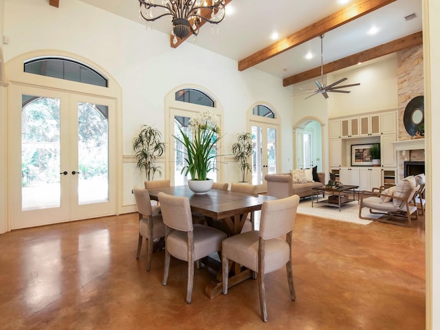 dining room with a towering ceiling, finished concrete floors, french doors, a fireplace, and beam ceiling