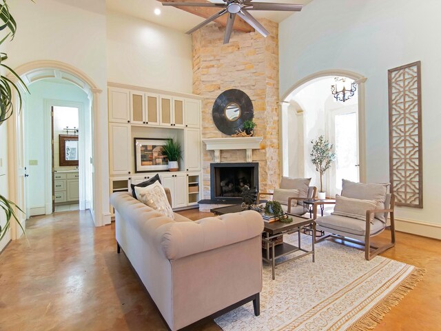 living room with ceiling fan with notable chandelier, a high ceiling, and a stone fireplace