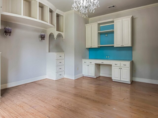 unfurnished office featuring ornamental molding, light wood-type flooring, built in desk, and a notable chandelier