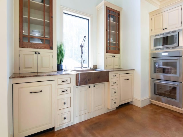 kitchen featuring baseboards, glass insert cabinets, finished concrete floors, stainless steel appliances, and a sink