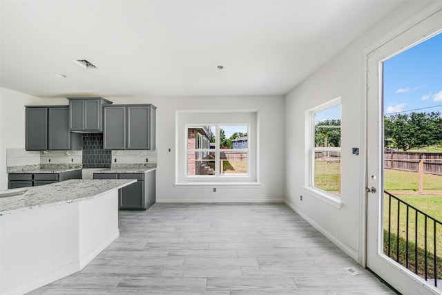 kitchen featuring gray cabinets, decorative backsplash, and light stone countertops