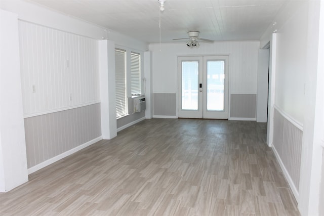 empty room with ceiling fan, wood walls, french doors, and light hardwood / wood-style floors