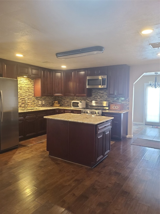 kitchen featuring a kitchen island, dark wood-type flooring, stainless steel appliances, backsplash, and dark brown cabinetry