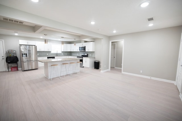 kitchen featuring appliances with stainless steel finishes, decorative backsplash, white cabinets, a kitchen island, and a breakfast bar area