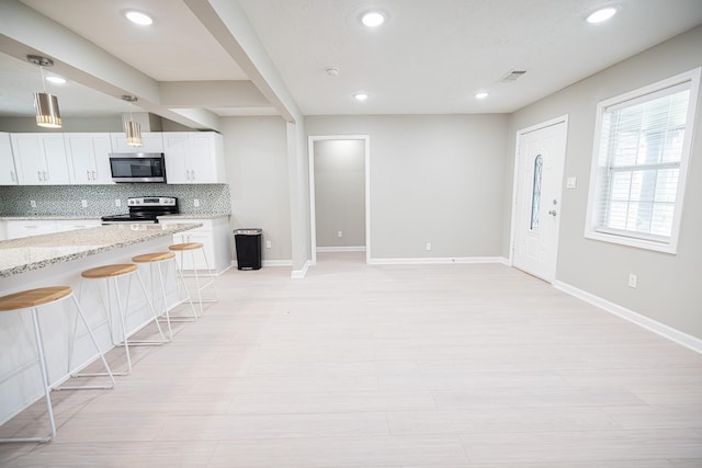 kitchen with tasteful backsplash, a breakfast bar, white cabinetry, light stone countertops, and stainless steel appliances