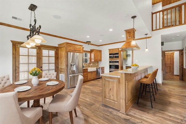 kitchen featuring pendant lighting, kitchen peninsula, stainless steel appliances, crown molding, and light stone countertops