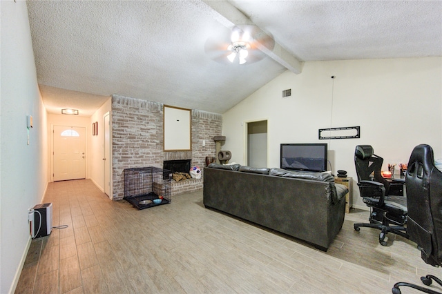 living room featuring a textured ceiling, light hardwood / wood-style flooring, a brick fireplace, ceiling fan, and vaulted ceiling with beams