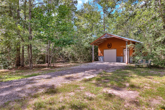 detached garage featuring driveway and a view of trees