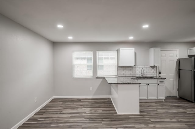 kitchen featuring light stone counters, a sink, white cabinetry, freestanding refrigerator, and decorative backsplash