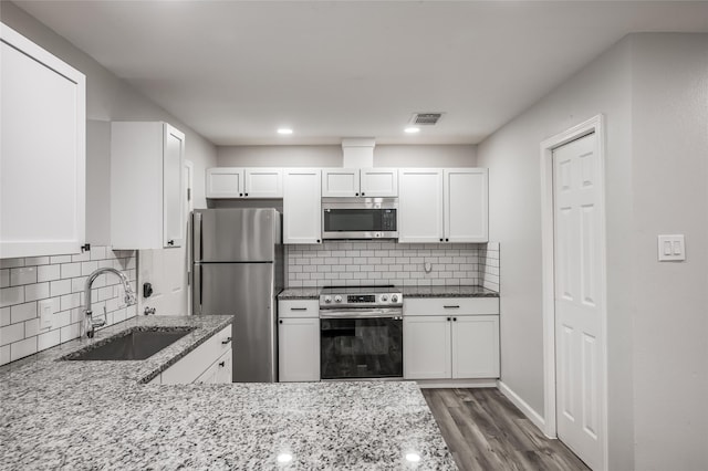 kitchen with light stone counters, visible vents, appliances with stainless steel finishes, white cabinets, and a sink