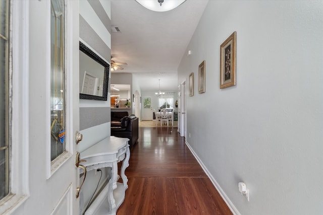 corridor with dark hardwood / wood-style flooring and an inviting chandelier