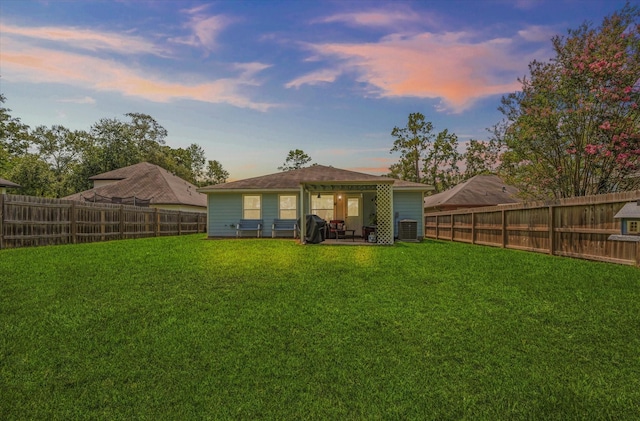 back house at dusk featuring central AC unit and a lawn