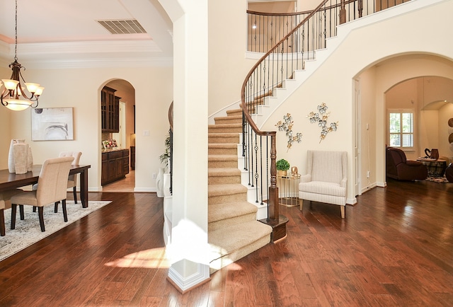 foyer featuring a high ceiling, crown molding, wood-type flooring, and a notable chandelier