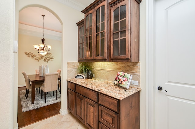 kitchen with light hardwood / wood-style floors, decorative backsplash, ornamental molding, light stone counters, and a notable chandelier