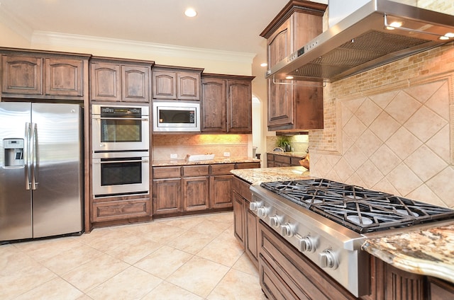 kitchen with appliances with stainless steel finishes, light stone countertops, tasteful backsplash, crown molding, and wall chimney range hood