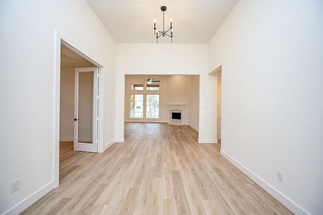 unfurnished living room featuring ceiling fan with notable chandelier, light hardwood / wood-style floors, and a premium fireplace