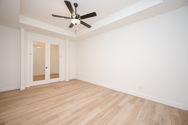 unfurnished room featuring ceiling fan, light hardwood / wood-style floors, a tray ceiling, and french doors