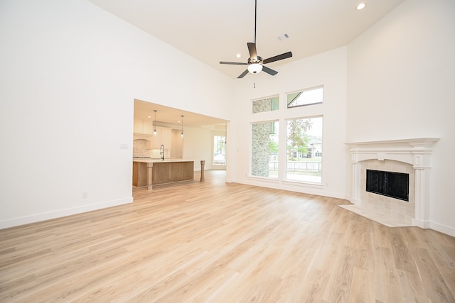 unfurnished living room featuring a towering ceiling, ceiling fan, sink, a fireplace, and light hardwood / wood-style floors