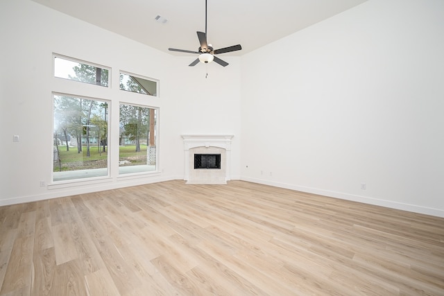 unfurnished living room featuring ceiling fan, a towering ceiling, a healthy amount of sunlight, and light wood-type flooring