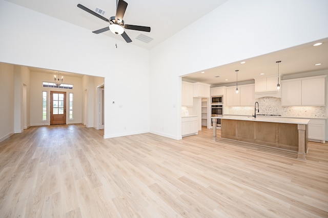 unfurnished living room with ceiling fan with notable chandelier, light wood-type flooring, and high vaulted ceiling