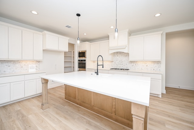 kitchen featuring a center island with sink, white cabinets, pendant lighting, and light hardwood / wood-style floors