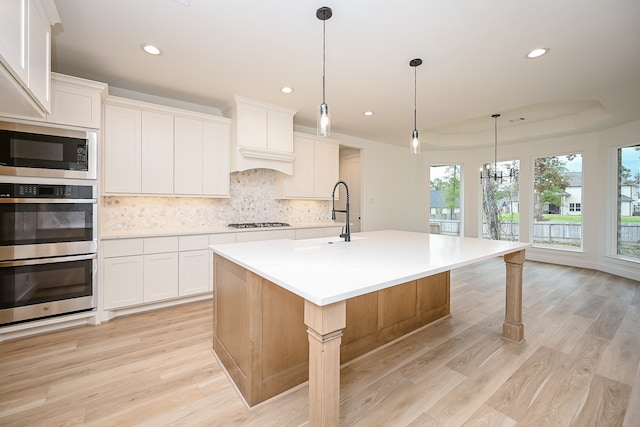 kitchen with a kitchen island with sink, decorative backsplash, light hardwood / wood-style floors, white cabinetry, and stainless steel appliances