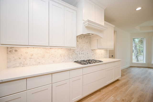 kitchen featuring white cabinets, stainless steel gas stovetop, light hardwood / wood-style floors, and tasteful backsplash