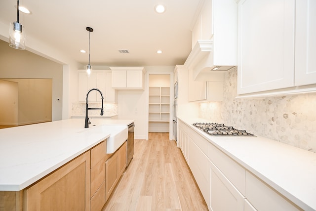 kitchen with white cabinetry, an island with sink, stainless steel appliances, and decorative light fixtures