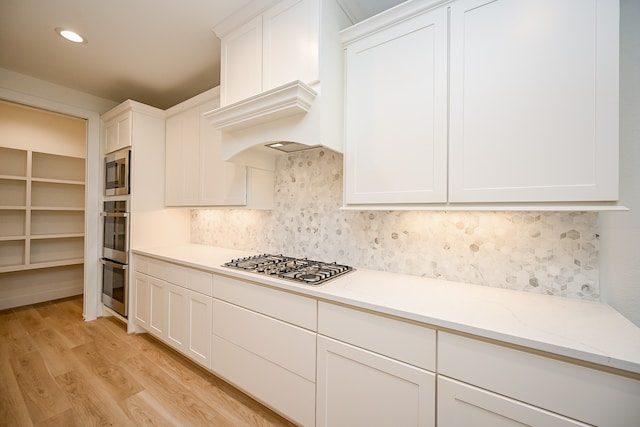 kitchen featuring white cabinets, light wood-type flooring, stainless steel appliances, and tasteful backsplash