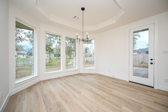 unfurnished dining area featuring light hardwood / wood-style floors, an inviting chandelier, and a tray ceiling