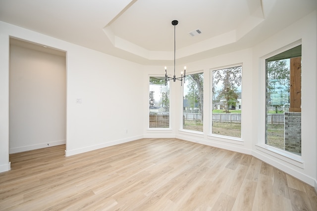 unfurnished dining area featuring a healthy amount of sunlight, a raised ceiling, light hardwood / wood-style floors, and a chandelier