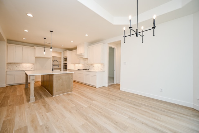 kitchen featuring tasteful backsplash, pendant lighting, light hardwood / wood-style flooring, white cabinetry, and an island with sink